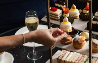 Person's hand picking up cake from Afternoon tea platter with glass of champagne