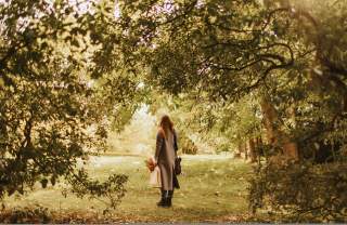 A woman surrounded by trees, looks up at the autumn leaves
