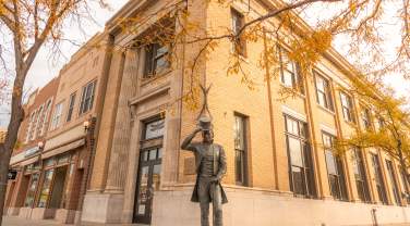 Historic brick building with autumn leaves in foreground. A statue of a President James Moore tipping his hat, creating a warm, nostalgic scene.