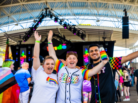 three friends cheering in front of a stage at pridefest