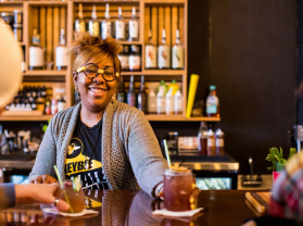 A bartender serving a non-alcoholic cocktail to two bar patrons.