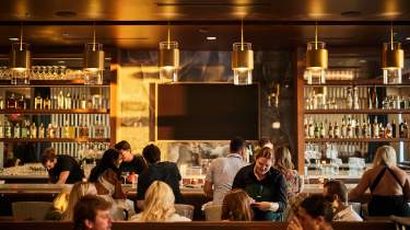 Warm lights glow over a bustling dining room with servers and diners.