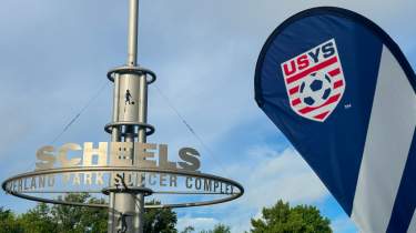 A US Youth Soccer banner waves in front of the Scheels Overland Park Soccer Complex sign