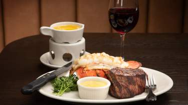 A delicious steak and lobster tail on a plate with a glass of wine to the side.