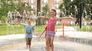A young girl and boy play in fountains of water at the Thompson Park Splash Pad in Overland Park, KS