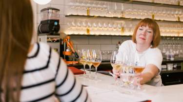 A woman serves a patron a wine flight on a white marble bar top.