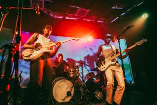 Band on stage with bright, colorful lights shining on them.