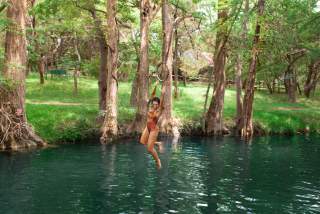 Image of a women jumping off a rope swing into Blue Hole in Wimberley, Texas.