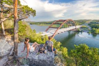 Hikers sitting on a hilltop rock overlooking the Pennybacker Bridge at Lake Austin.