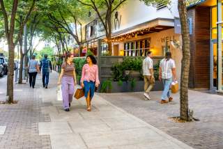 People walking on the sidewalk through the 2ND Street District chatting while holding shopping bags.