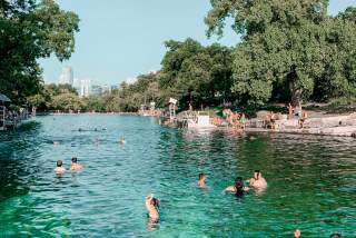 Adults and children playing in and along the banks of Barton Springs Pool.