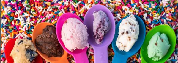 6 spoons all different colors with a scoop of ice cream sitting on each. Laying in a pile of sprinkles