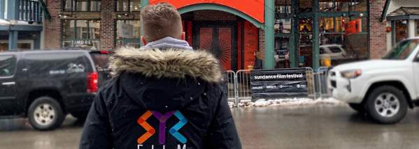 a man standing with a syr film office logo looking at a sundance film festival theater
