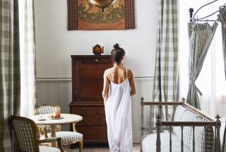 A woman in a white dress moves through a guest room at the upscale New Orleans boutique hotel Hotel Peter and Paul in the Marigny.