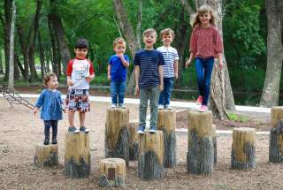 kids standing on tree stumps at varying heights in a park