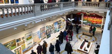 Lots of people looking at art work in a large galley with a balcony