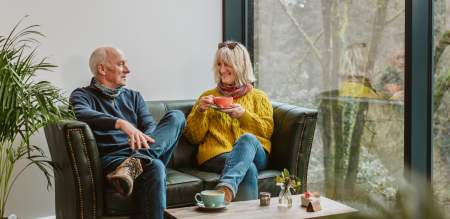 Older couple sitting on coffee shop sofa drinking cups of coffee