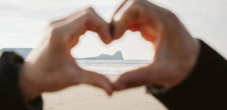 A close up of a pair of hands making a heart shape with Worm's head visible in the distance in the centre of the heart shape.