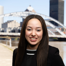 Woman standing in front of bridge in downtown Rochester wearing a black blazer with hand in her pocket