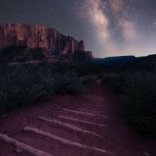 Starry Skies over a dirt hiking trail with logs laid out for steps and towering crimson cliffs in the background in Kolob Canyons, Ut.