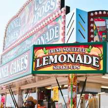 A man stands under a food kiosk that reads lemonade