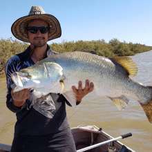 A man in a tinny holding a freshly caught barra, in a creek near Port Hedland