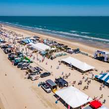 Aerial shot of a long stretch of beach covered in tents and people during a festival.