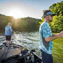 Two men hold fishing poles off a boat in the middle of the river