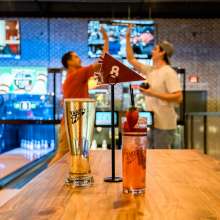 two guys high-fiving in a blowline alley with drinks in the foreground