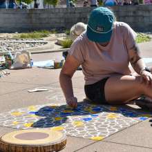 woman creating a large chalk graphic on a sidewalk