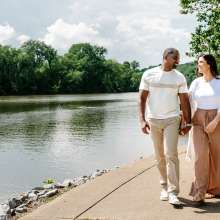 a man and woman walk along a riverside path