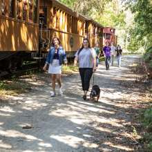 two people walking on rail trail with their dog next to northern central railway of york's steam engine