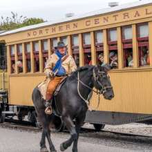 cowboy riding a horse next to a northern central railway train