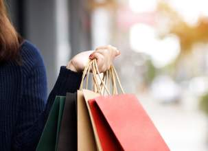 Picture on a persons hand holding shopping bags with a blurry street view in the background.