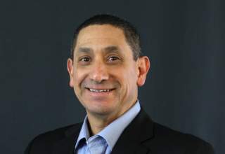 A formal headshot of Jared Vasquez, dressed in a black suit jacket and light blue dress shirt.