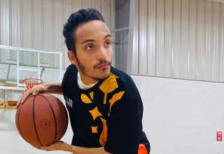 Nate Dickerson poses for a photo in an empty basketball gym, holding the ball in his hands while looking intensely to the right.
