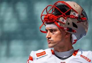 Jakob Sullivan looks across the field dressed in his white and red Berlin football jersey with his helmet propped up on the top of his head.