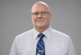 A formal headshot of Craig Nowotny, wearing a white dress shirt and a black and blue stripe tie.