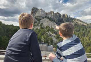 two kids sitting on the grand view terrace at mount rushmore pointing at the memorial
