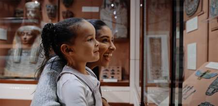 A small girl and woman looking inside an Egyptian artifact display cabinet.