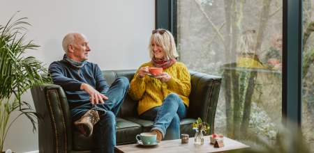 Older couple sitting on coffee shop sofa drinking cups of coffee
