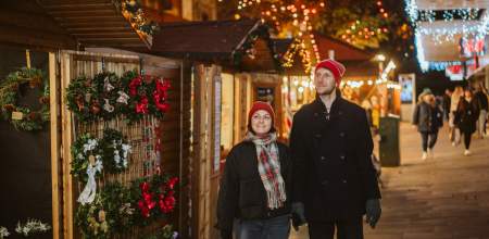 Young couple holding hands and exploring Swansea Christmas Market at night