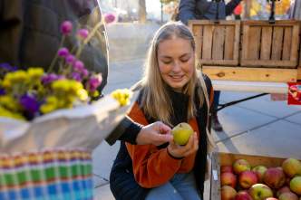 A white woman looks at an apple she picked out of a basket at the farmers' market