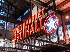 Neon sign reading ‘3rd Street Market Hall’ with a glowing star, inside a modern industrial-style building with glass walls and metal beams.