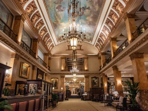 Grand hotel lobby with ornate chandeliers, marble columns, and a painted ceiling mural, creating an elegant and historic atmosphere.