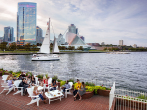 a group of people eating on the patio in front of the Milwaukee skyline with a sailboat in the harbor