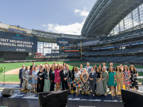 Group photo of attendees at Visit Milwaukee's Annual Meeting, posed on a stage at American Family Field (Milwaukee Brewers stadium) with stadium seating and banners visible in the background.
