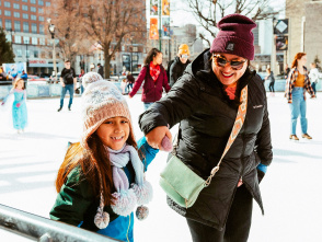 a little girl ice skating on a public ice rink while holding her mom's hand