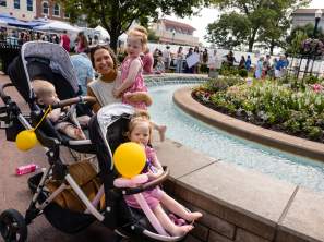A family with a stroller and balloons in front of the fountain on the Bentonville square.