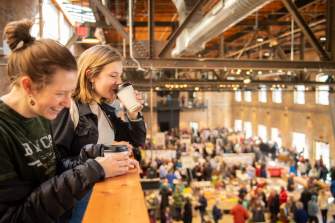 Two women sip coffee and laugh while overlooking the Late Winter Farmers Market at Garver Feed Mill